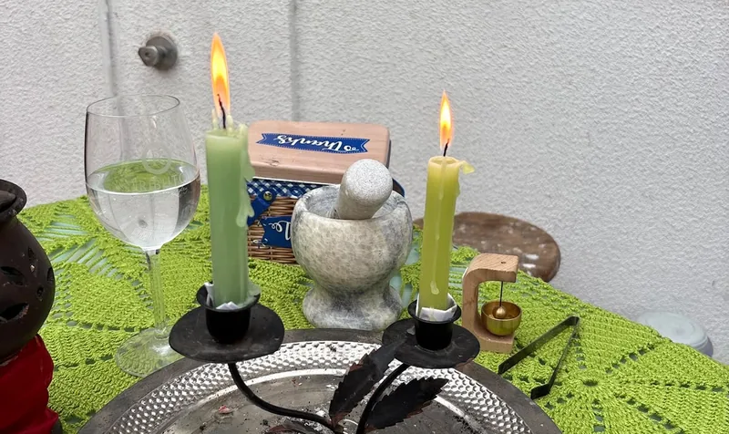 Dos velas encendidas, una copa de agua y un mortero de piedra sobre un mantel verde